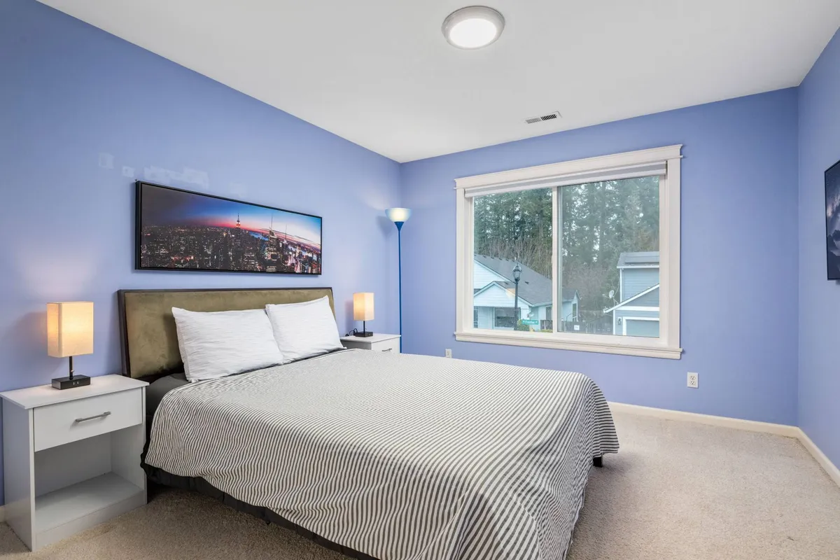 A cozy bedroom scene with a striped bed, a decorative cityscape photograph above the headboard, and soft natural light filtering through a window, evoking a sense of tranquility and comfort.