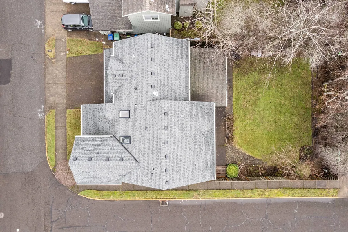This image captures the peaceful exterior of the home with a view of the roof structure, surrounding greenery, and the driveway, suggesting an inviting and safe environment. The open space is suitable for children to play and families to gather outdoors.