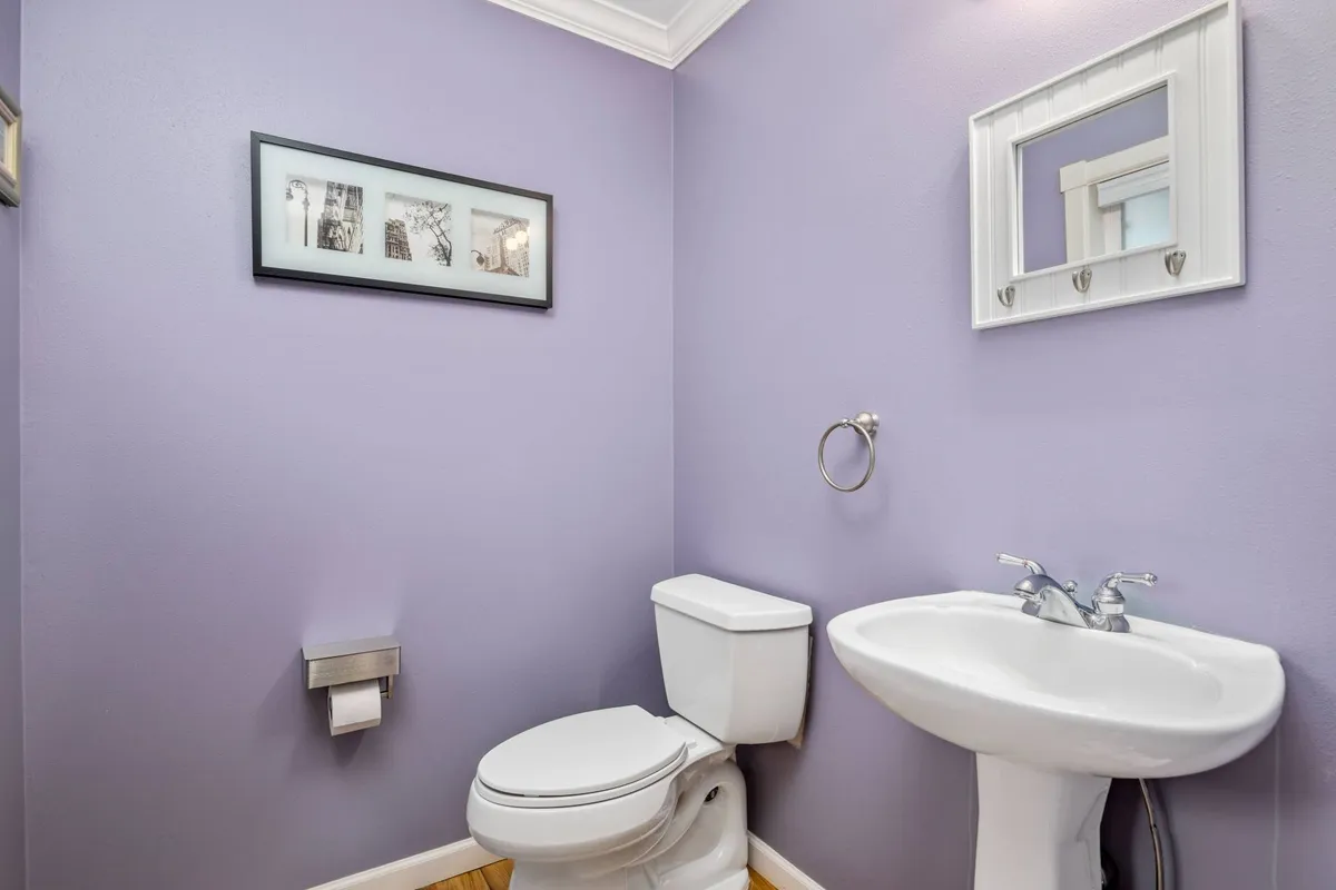A compact half bath with inviting purple walls, a framed artwork, and functional features like a sink and toilet. The cheerful design and accessibility make this an ideal convenience for guests during gatherings.