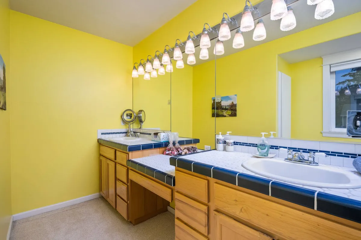 A fresh, uplifting bathroom with yellow walls, a large mirror, modern light fixtures, and a spacious sink area. The mood is bright and welcoming, perfect for morning routines and self-care.