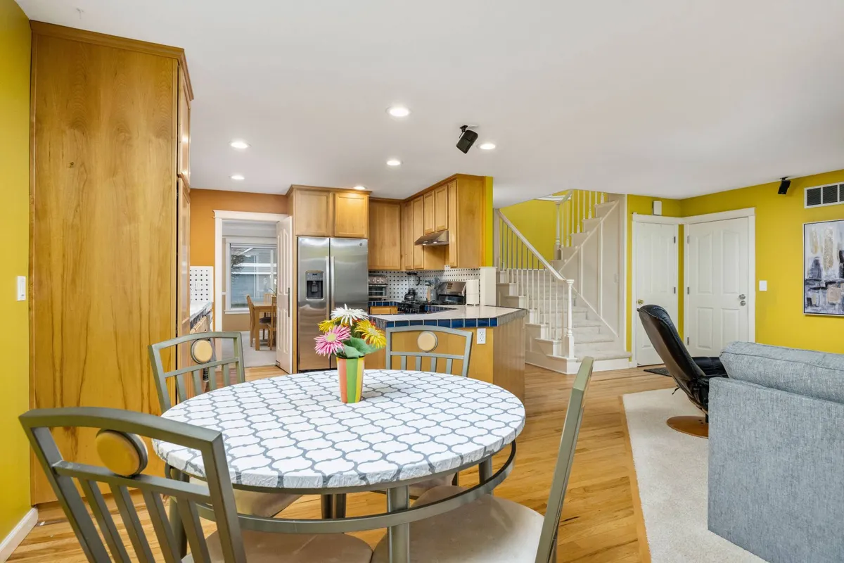 The photo spotlights a round dining table adjacent to a kitchen island, with a staircase visible in the background. The space is inviting and cozy, encouraging family meals, casual gatherings, and shared moments. Natural light streams in, adding to the warm ambiance and sense of openness.