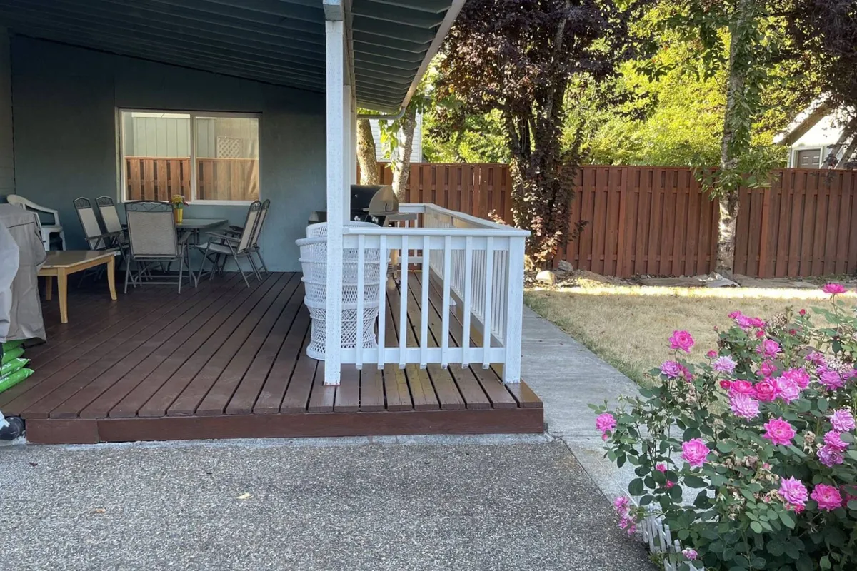 A close-up of the deck area in the backyard, featuring outdoor seating, a grill, and blooming pink roses. The setup invites relaxation, outdoor dining, and entertaining guests in a secure, natural setting—showcasing how the backyard can serve as a haven for all guests, not just kids and pets.