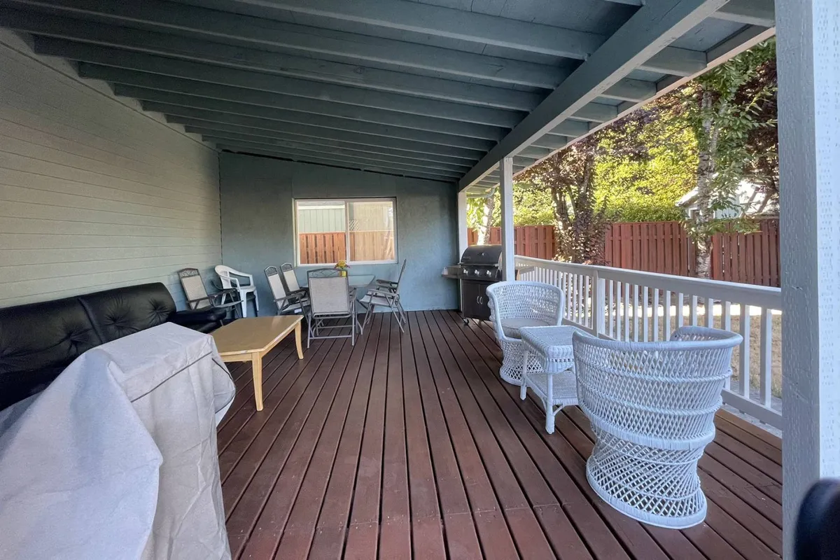 This image showcases a cozy outdoor dining area with wicker chairs, a wooden table, and a grill, set on a patio likely connected to the backyard. The space is bathed in natural light during sunset, suggesting a welcoming and comfortable area for relaxing and social gatherings.