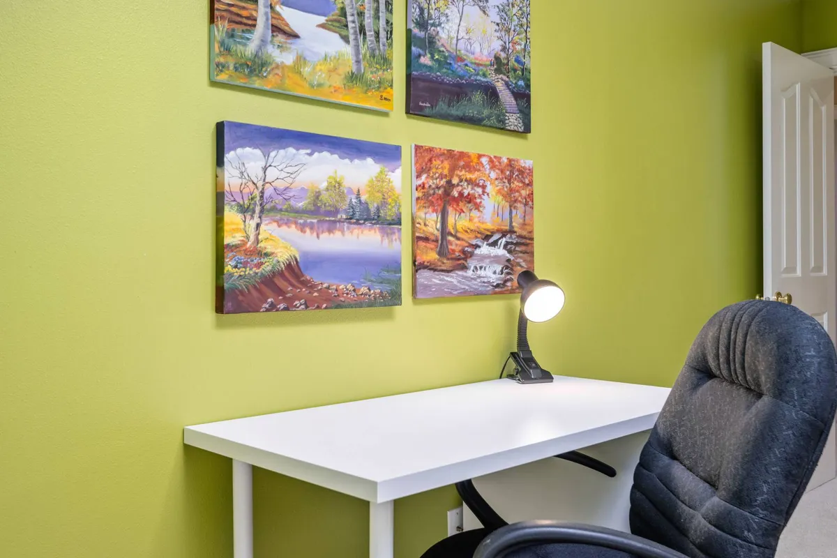 A well-lit workspace featuring a desk, lamp, and inspiring artwork, set in a quiet and uncluttered room. The setup offers a focused environment ideal for working, studying, or engaging in creative pursuits.