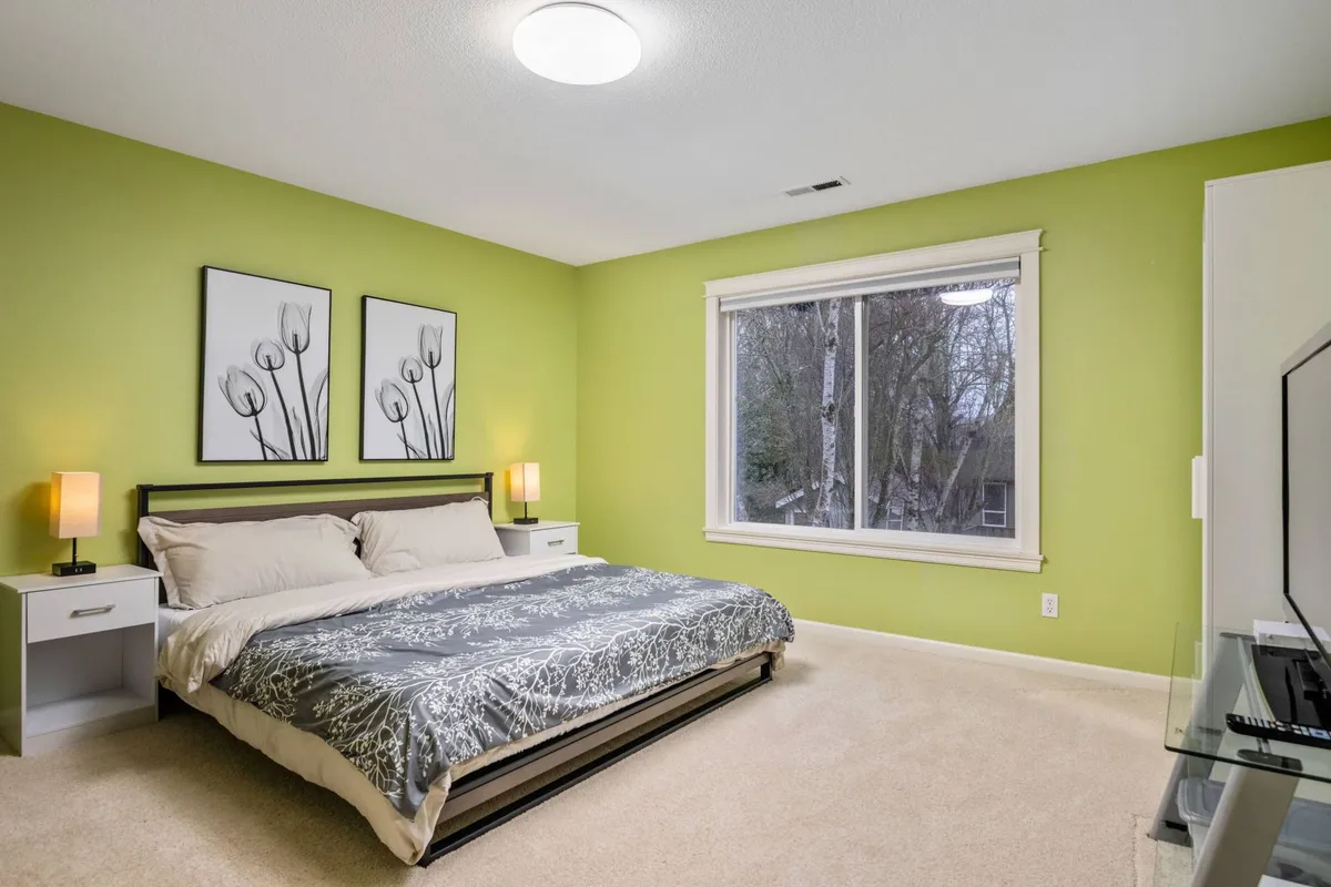 A tranquil bedroom with a comfortable bed, large window streaming in natural light, and artistic decor, creating an inviting and restful environment.