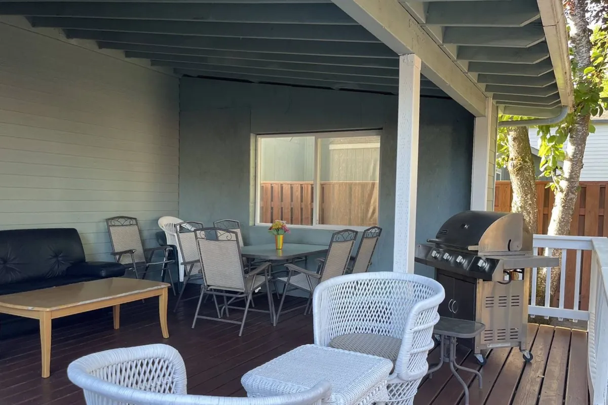 An outdoor seating area with a grill, table adorned with flowers, and ample seating for gatherings. The casual, welcoming vibe hints at memorable family barbecues, outdoor meals, and relaxing afternoons together.