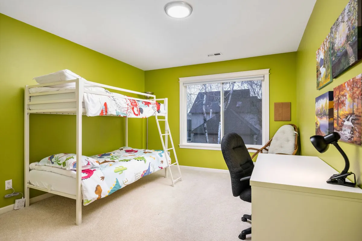 A playful bunk room showcasing a bunk bed, a colorful desk and chair, bright window light, and fun wall art. The room is clearly designed for kids or remote workers, offering both restful and creative spaces.